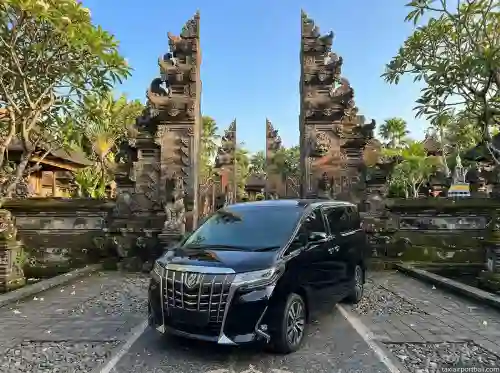 Black Toyota Alphard private car in front of a Balinese gate